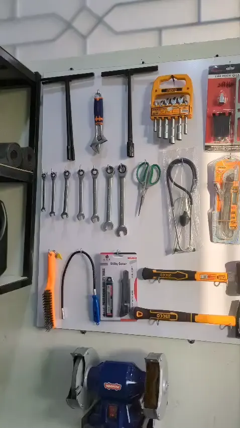 Pegboard of spanners, pliers and hammers above a bench grinder